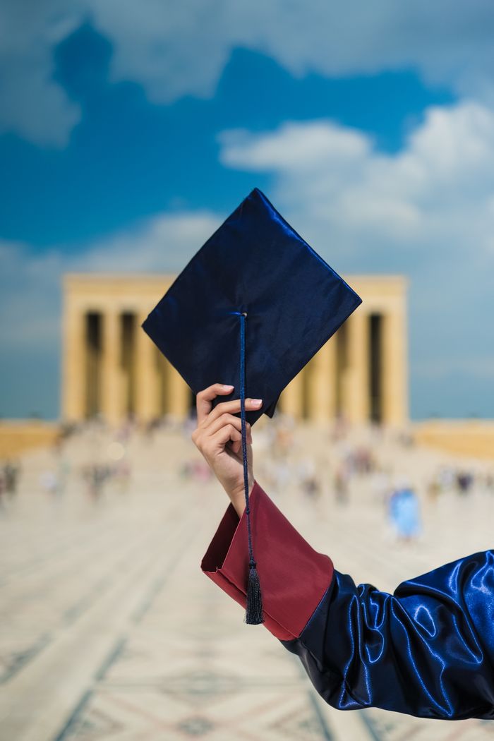 A graduate holding a cap in front of a blurred architectural background, symbolizing achievement.